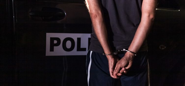 criminal with handcuffs in front of a police car.