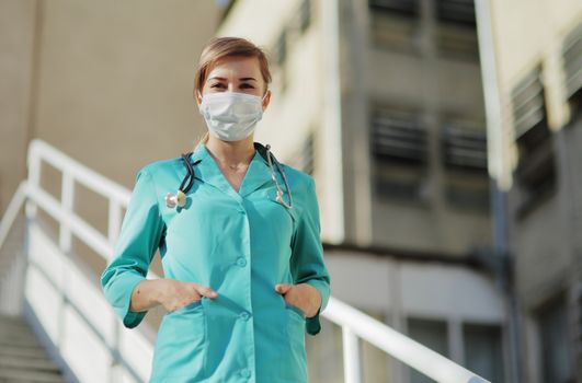 Female doctor or nurse in a protective face mask walking up the stairs. Safety measures against the coronavirus. Prevention Covid-19 healthcare concept. Stethoscope over the neck. Woman, girl.