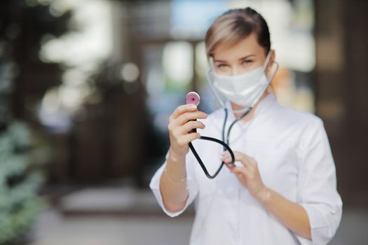 A woman doctor in a face protective medical mask with a stethoscope ready to check lungs. Safety measures against the coronavirus. Prevention Covid-19 healthcare concept. Girl.