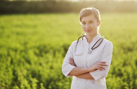 Portrait of a beautiful female doctor or nurse on green grass background. Prevention Covid-19 healthcare concept. Stethoscope over the neck. Woman, girl.