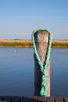 An old wooden bollard or pole with a rope near a pier at the Baltic Sea