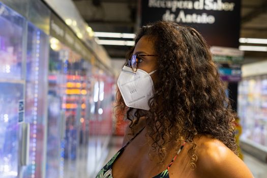 Brazilian young woman shopping in the supermarket with mask. New normality concept.
