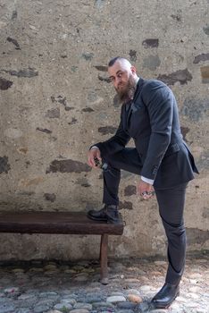 Man in elegant clothes rests one foot on a wooden bench in a small village