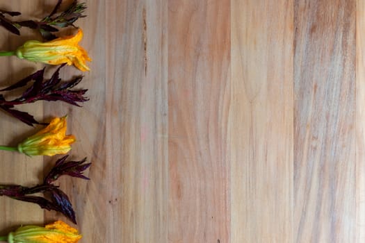 Wooden background with pumpkin flowers and purple epazote, for copy space. Food background