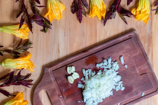 Wooden background with pumpkin flowers and purple epazote, with cutting board for vegetables and chopped onion. Food background