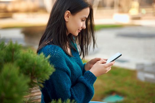 Side view portrait of adorable young student looking at smartphone screen outdoors