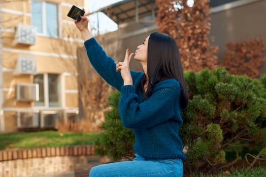 Side view of a pretty female student taking self picture outdoors with a small fluffy conifer on background