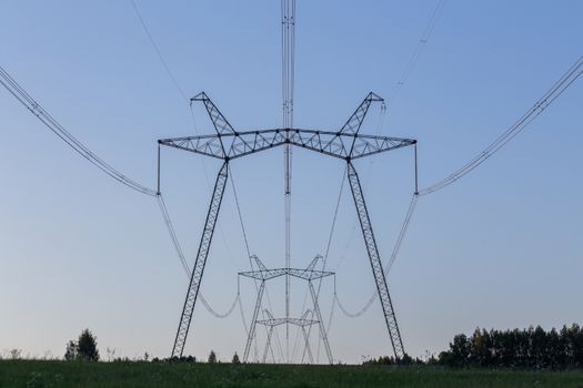 huge power line towers on field at summer evening.