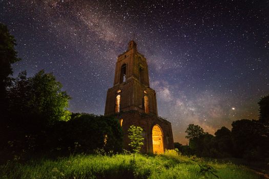 night brick bell tower ruin in forest at starry night with mystical internal light.