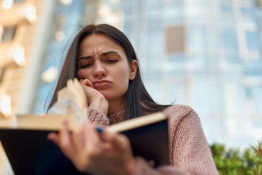 Upset and distressed female brunette is reading book in city street