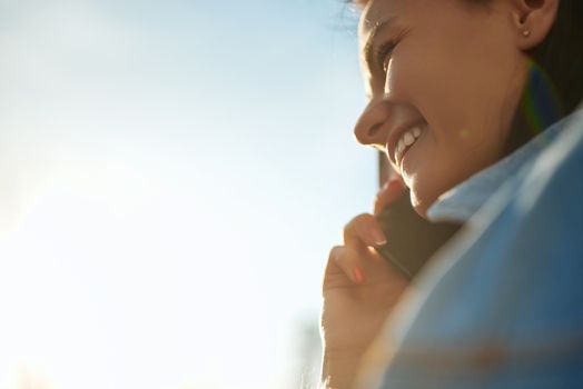 Cropped shot of a young pleasant woman communicating by phone opposite light blue sky