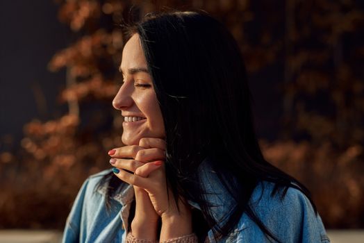 Lovely young long-haired woman clasping her hands with heartwarming smile on a walk in a park