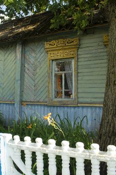 Traditional ornamented yellow open shutters of an old wooden rural house in the village of Belarus. Old shabby teal house