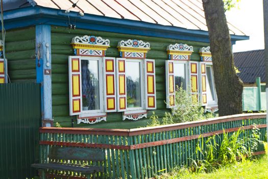 Colorful windows with carved platbands on the decorated facade of the wooden house. Village in Belarus
