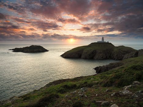 Dramatic sunset view of Strumble Head Lighthouse built by Trinity House in 1908 on the top of the island of Ynys Meicel with orange clouds overhead, Pembrokeshire Coast National Park, Wales, UK