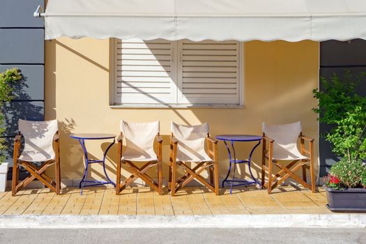 Traditional greek street cafe. Empty tables and chairs of a street cafe. Cafe, tavern exterior. Tourist places. Hotel, resort waiting for visitors, customers, clients. Tourism business concept