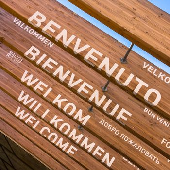 The word welcome in multilingual applied on the wooden beams of a pavilion.