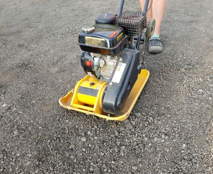 Worker is using vibrating plate compactor for ground road compaction.