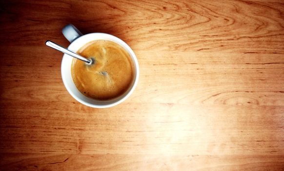 Top down view of cup with espresso and spoon on a brown table.