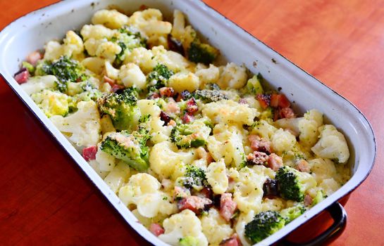 Baked Cauliflower and Broccoli with Grated Parmesan and Pieces of Bacon in Black Pan.