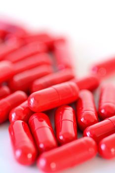 Heap of a red capsules spilled out on the white background.