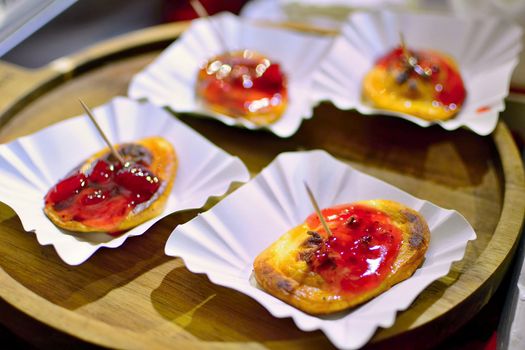 Four portions of grilled oscypek (traditional smoked cheese made of sheep milk) with cranberries serving on wooden plate.