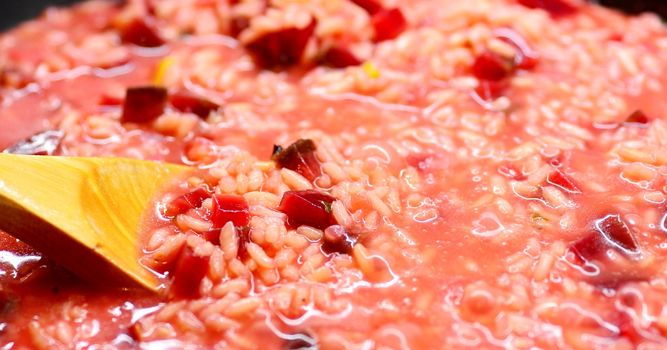 Close-up of an Italian Creamy Beetroot Risotto and Stirring Wooden Spoon.