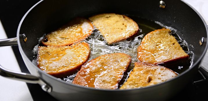 A frying of bread in hot oil in black pan close up.