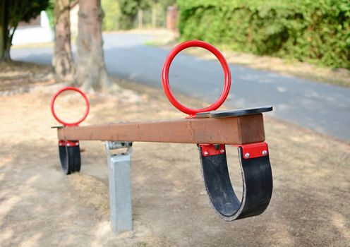 A close-up of empty brown wooden swing seat with red handles in the playground. Shallow depth of field. Focused on foreground.