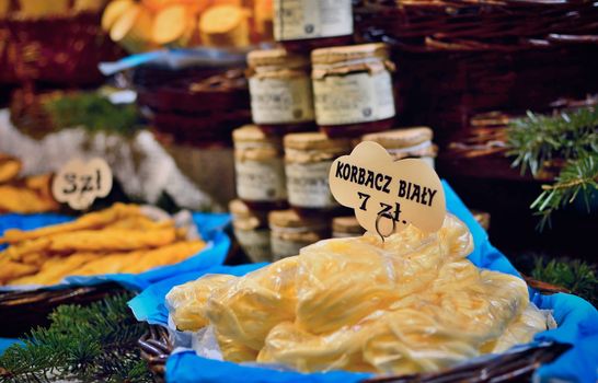 Closeup of smoked cheese with price tags and other food on outdoor stand on traditional Poland market.