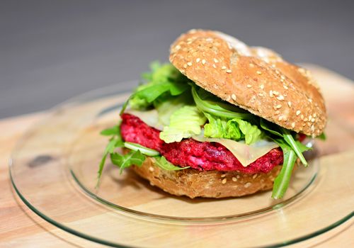 Closeup of beetrot burger with grilled arugula on wooden plate.