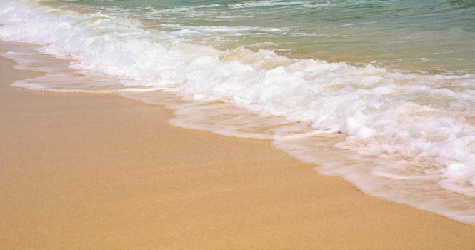 Closeup of a gold sand beach with turquoise ocean water with waves.