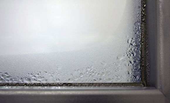 Closeup of the winter condensation on the inside of a window, insulation failure. A window glass covered with condensation drops.