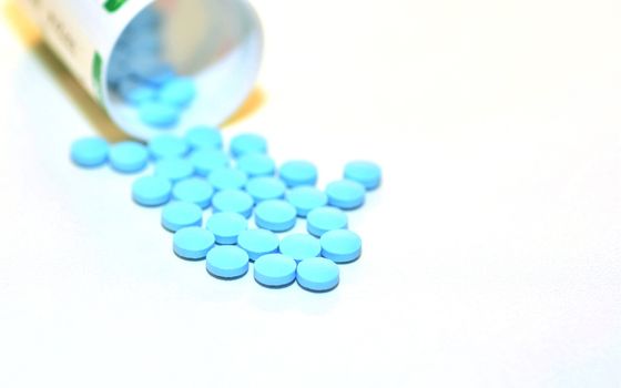 Closeup of a Blue Drug Pills Spilling Out of a Bottle on the White Background.