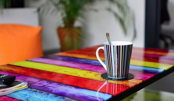 Multicolor glass table with cup of coffee in modern furnished living room. Focused on foreground with cup of coffee.