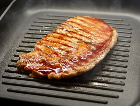 Fresh Grilled Beef Steak in Steam and Smoke on the Iron Grill Pan.