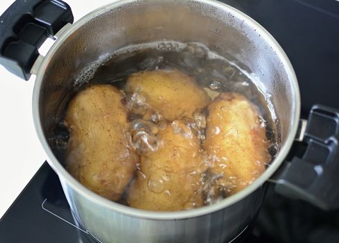 Top view of boiling whole potatoes in hot water in silver saucepan.