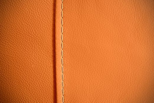 Full frame background texture of pebbled orange leather with one seam thread.
