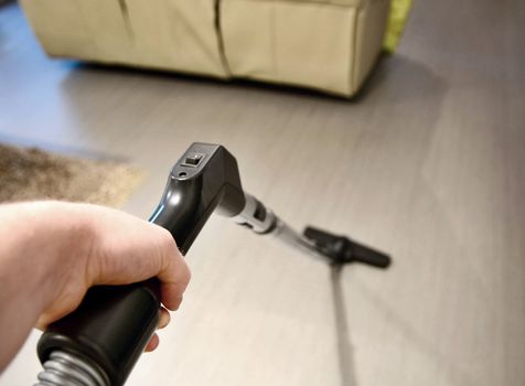 Man hand holding vacuum cleaner tube and makes housework and vacuuming the floor in room. Closeup point of view or first person view shot.