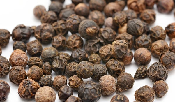 Closeup of whole black peppercorns on white background.