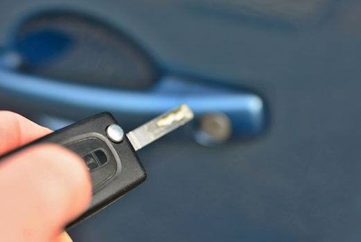 Closeup of hand holding a remote key unlocking the blue car.