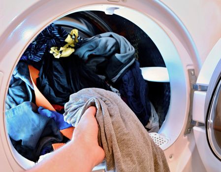 Closeup of hand holding and put washed laundry into tumble clothes dryer machine.