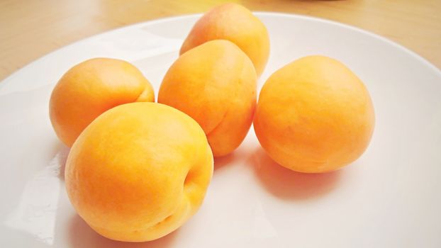 Group of five apricots on a white plate.