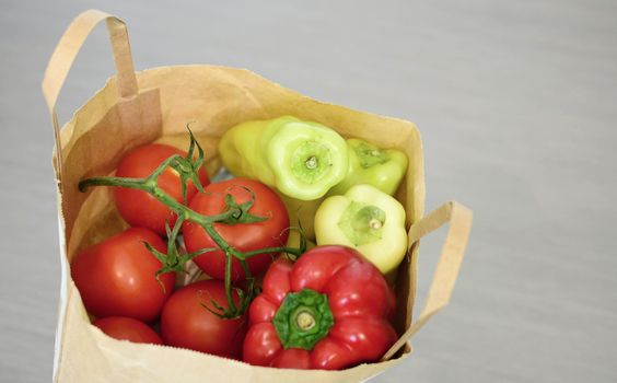 Top view of grocery paper bag full of tomatoes and green peppers on grey background.Full paper bag with vegetables.