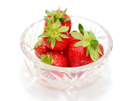 Heap of fresh strawberries in glass bowl over white background.