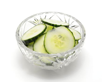 Heap of fresh cucumber slices in glass bowl over white background.