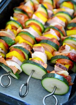 Pan full of metallic skewers with uncooked raw pork meat and vegetables ready for baking.