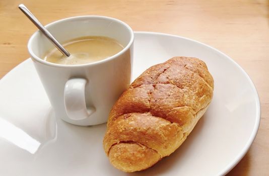 Breakfast with coffee and fresh croissant on a white plate.