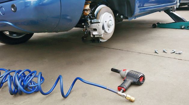 View of a disc brake during tyre replacement and pneumatic air screwdriver on the ground. Car maintenance.