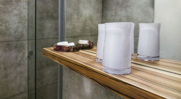 Bathroom wooden shelf with decorative candela glasses and soaps.